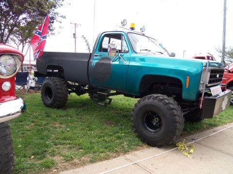 1989 Ford Bronco - A heavily modified pickup truck is parked on grass next to another vehicle.
