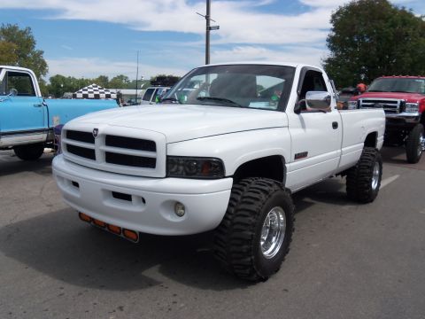 1989 Ford Bronco - A lifted white Dodge Ram pickup truck is parked outdoors with other vehicles visible.
