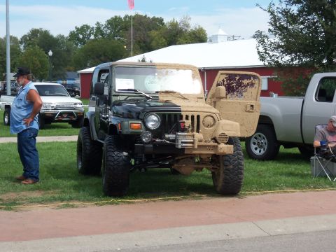 1989 Ford Bronco - This Jeep Wrangler is half clean and half covered in mud, parked at an outdoor event.