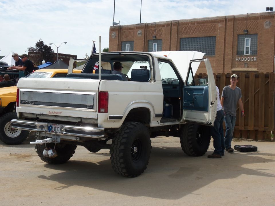 White 1989 Ford Bronco with lifted suspension, large tires, and open doors