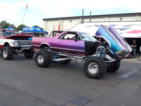 1989 Ford Bronco - Two custom lifted vehicles, a purple El Camino and a red and white truck, are parked side-by-side outdoors.