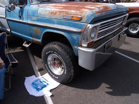 1989 Ford Bronco - A weathered blue Ford truck with a chrome bumper and BFGoodrich tires is parked next to another vehicle.