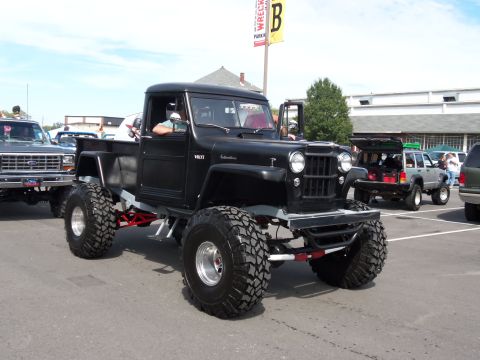 1989 Ford Bronco - A heavily modified black pickup truck with oversized tires is parked in a lot, with other vehicles visible in the background.