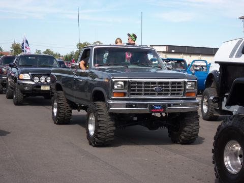 1989 Ford Bronco - A lifted Ford pickup truck is seen in a parade with other off-road vehicles.
