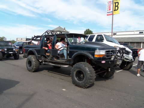1989 Ford Bronco - This heavily modified Ford Bronco features oversized tires and a custom bumper, with other vehicles visible in the background.