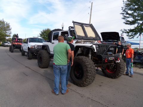 1989 Ford Bronco - Several modified off-road vehicles are lined up, with a white Jeep Wrangler prominently displayed with its hood open.