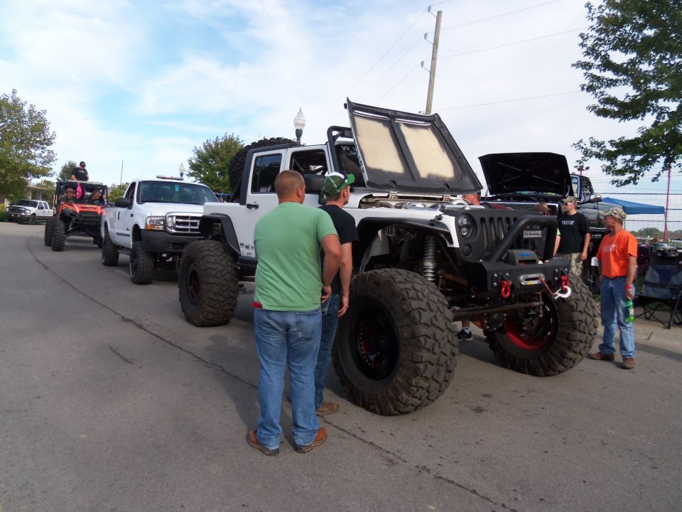 Modified white Jeep Wrangler with hood open, large tires, and custom bumper