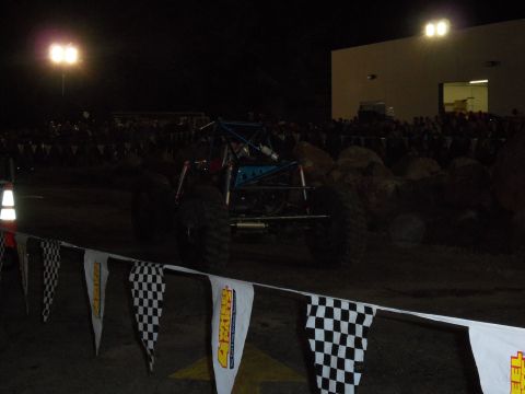 1989 Ford Bronco - A custom off-road buggy with a roll cage is seen from the rear at a nighttime event with spectators in the background.