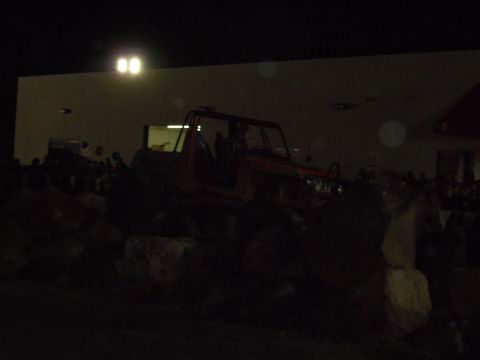 1989 Ford Bronco - An off-road vehicle is positioned on large rocks under bright lights at night.