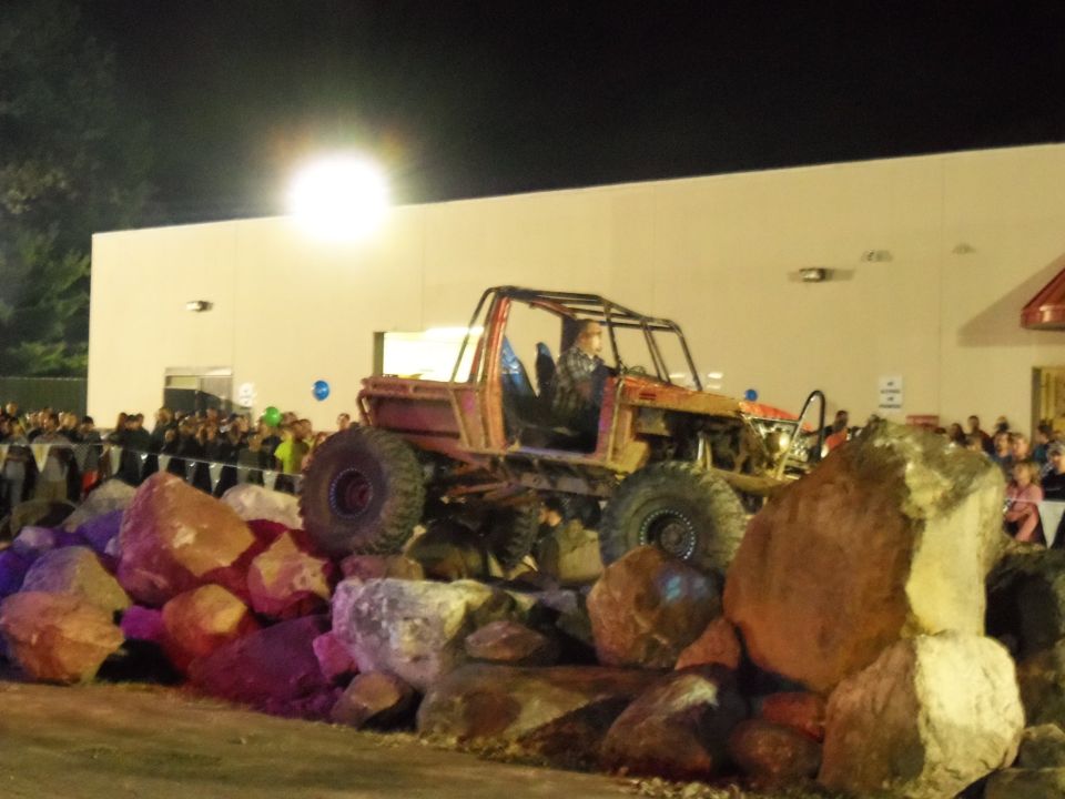Modified off-road vehicle with a roll cage, large tires, and exposed engine, climbing over rocks