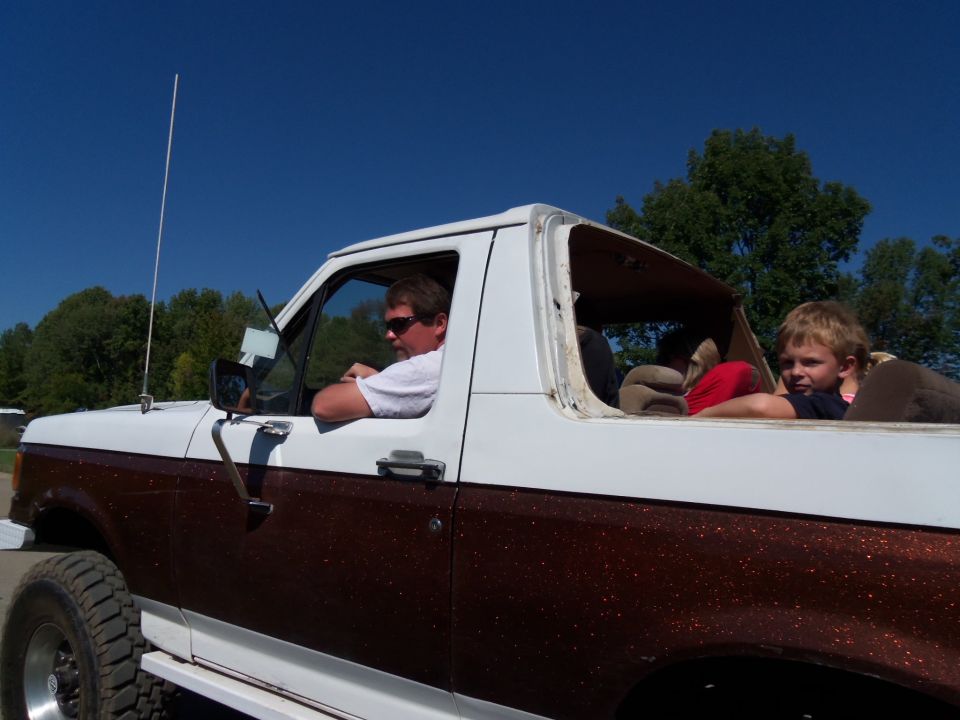 Man driving a white and brown Ford Bronco with a kid in the back