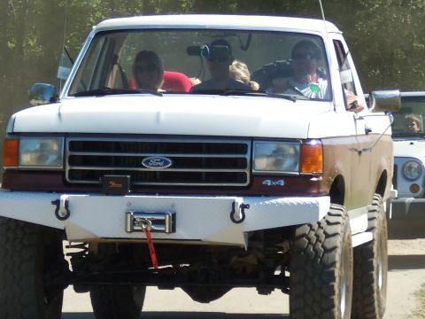 1989 Ford Bronco - This modified Ford Bronco features a custom bumper and large tires, with occupants visible inside.
