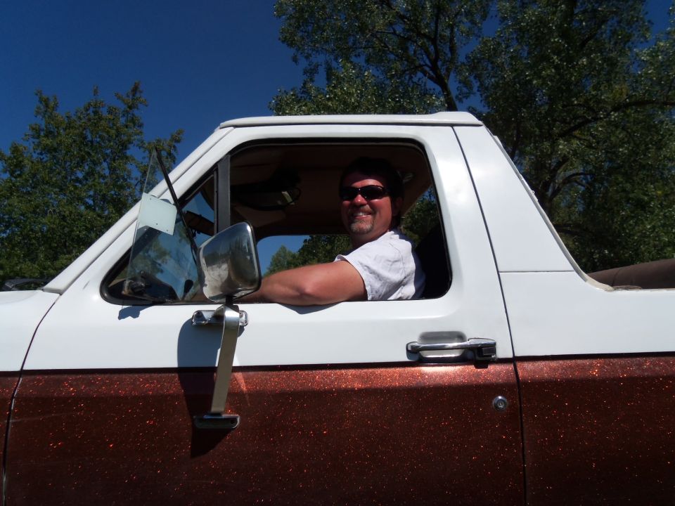 1989 Ford Bronco side view with driver smiling, white cab and brown speckled lower body