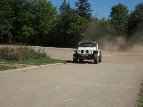 1989 Ford Bronco - A white Jeep Wrangler navigates a dusty turn on a paved and dirt road.