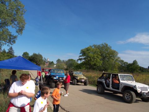 1989 Ford Bronco - Several Jeeps are parked on a road with people gathered around, under a clear blue sky.