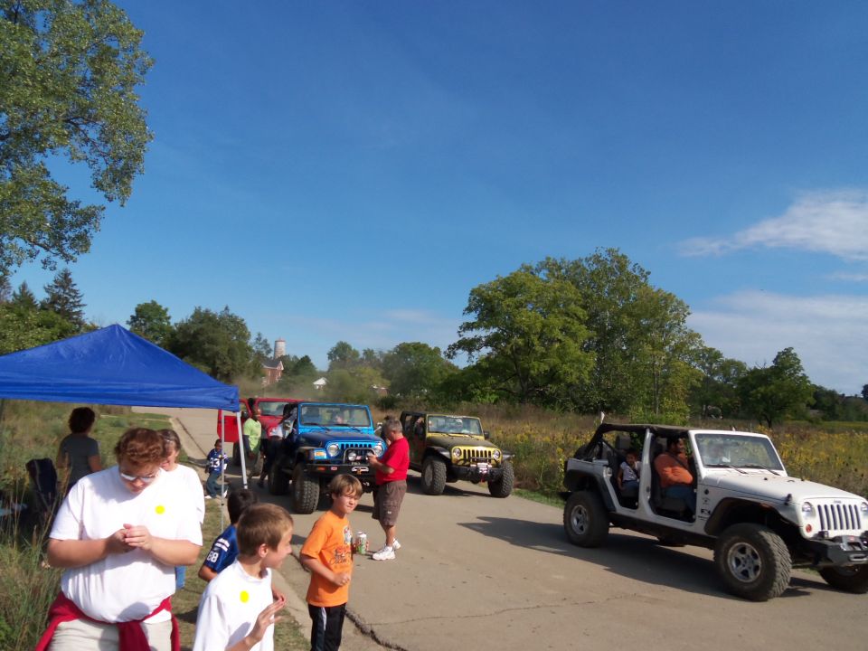White Jeep Wrangler parked on a road with people inside, blue and tan Jeeps behind it