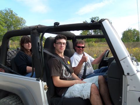 1989 Ford Bronco - Three people ride in a Jeep Wrangler on a sunny day with a field in the background.