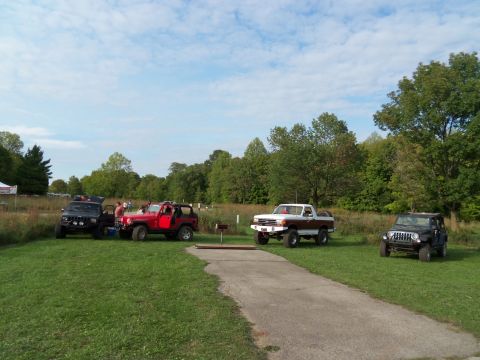 1989 Ford Bronco - A white and brown pickup truck with a lifted suspension is parked on the grass next to a paved path, with other vehicles visible in the bac…