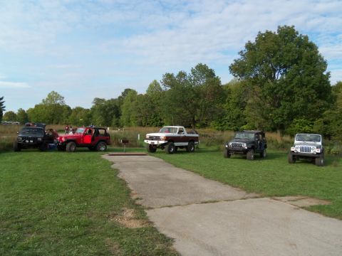 1989 Ford Bronco - A group of off-road vehicles are parked on a grassy area with trees in the background.