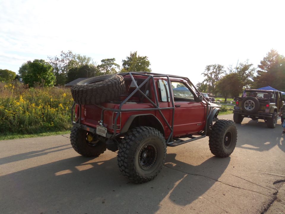 Red off-road vehicle with external roll cage and spare tire on back, seen from rear-3/4 angle