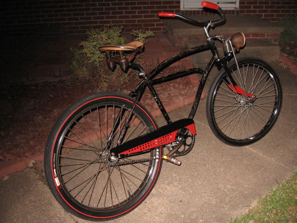 Black cruiser bicycle with red accents on wheels and chain guard, tan leather seat, and brown headlight