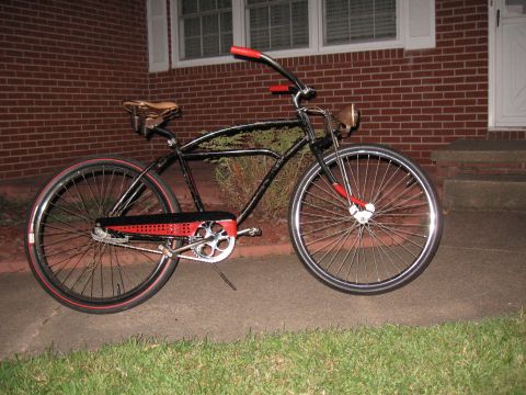 1994 Ford Bronco - A black cruiser bicycle with red handlebars and accents is parked on a sidewalk in front of a brick house.