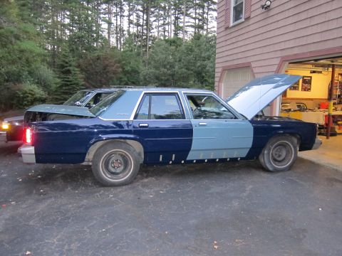 1991 Ford LTD Crown Victoria - A blue sedan with its hood and trunk open sits in a driveway next to another vehicle.