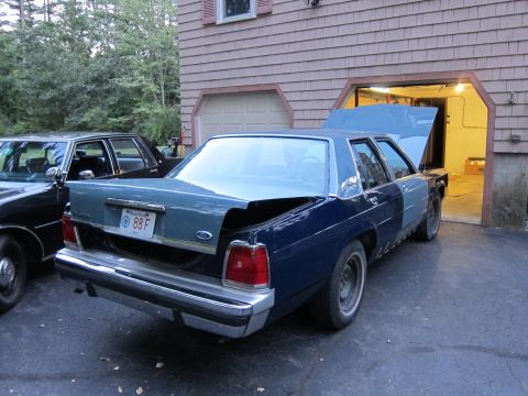 1991 Ford LTD Crown Victoria - Two sedans are parked in a driveway next to a house with an open garage.
