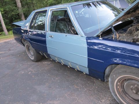 1991 Ford LTD Crown Victoria - This sedan displays a patchwork of blue paint and unfinished body repairs, indicating a project in progress.