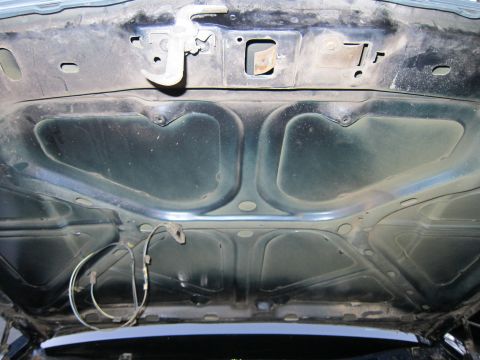 1991 Ford LTD Crown Victoria - Underside of a dark green hood, showing the latch mechanism and some wiring, with a hint of the car's bodywork visible below.