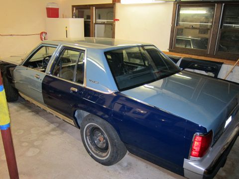 1991 Ford LTD Crown Victoria - A two-tone Ford Crown Victoria is parked indoors, showing primer on the front fender and dark blue on the rear quarter panel.