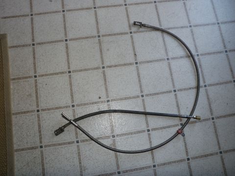 1961 International Scout 800 - Two flexible fuel lines, likely for a vehicle's fuel system, are laid out on a tiled surface.