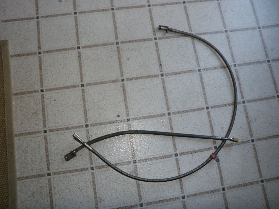 Two flexible fuel lines with metal fittings on a tiled floor