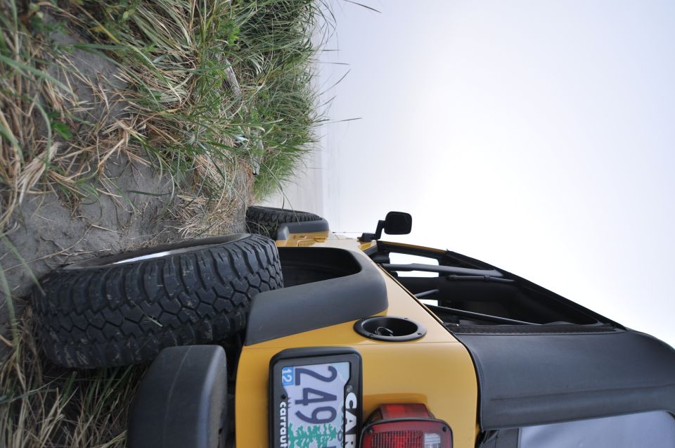 Yellow 2004 Jeep TJ on its side with grass and water in background. License plate visible