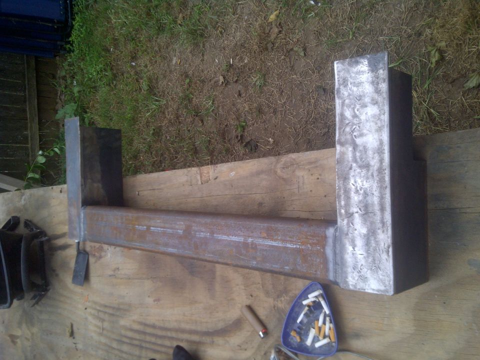Metal frame with welded uprights on a wooden surface, next to an ashtray with cigarette butts