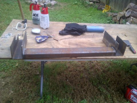 1995 Ford Bronco - Metal fabrication parts, including a U-shaped bracket and a long bar, are laid out on a wooden table with two spray bottles and tools nearb…