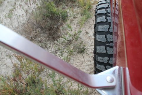 1990 Ford Bronco - Off-road tire and red vehicle side panel against a dry, sandy backdrop.