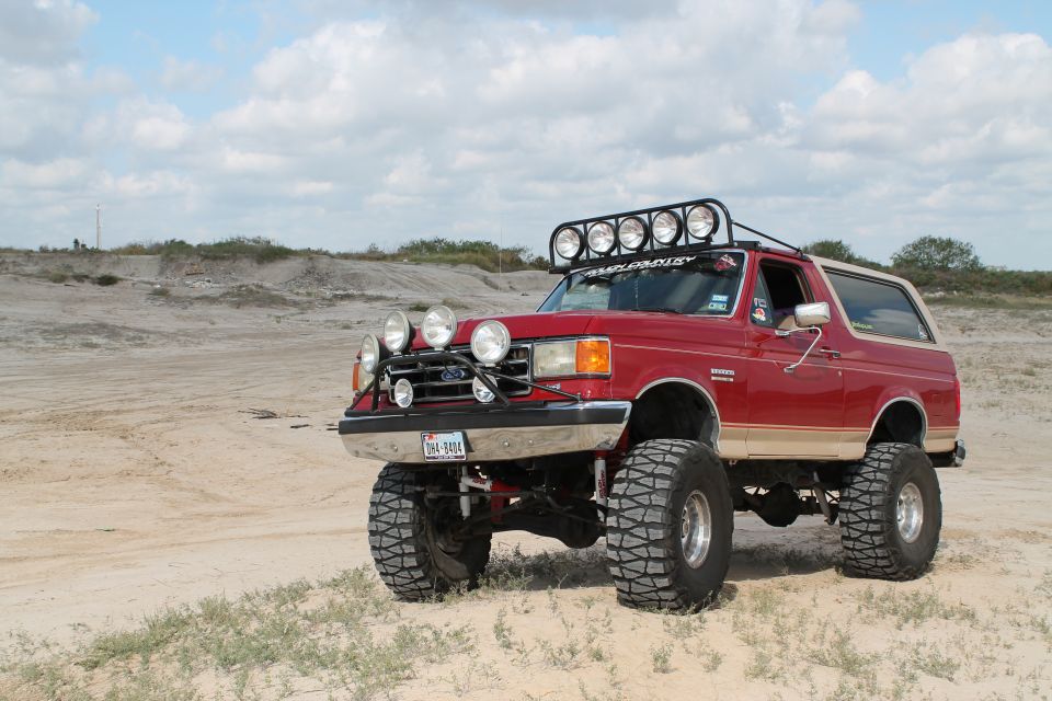 Red 1990 Ford Bronco with tan trim, lifted suspension, and multiple off-road lights