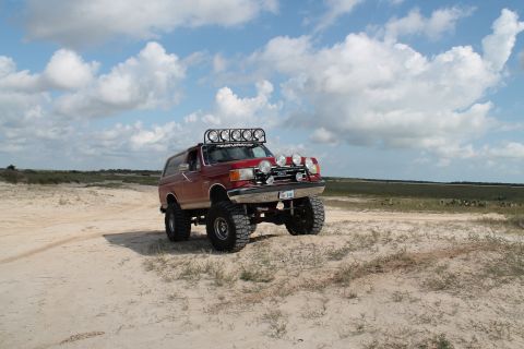 1990 Ford Bronco - Modified 1990 Ford Bronco with extra lights and large tires parked on a sandy trail.
