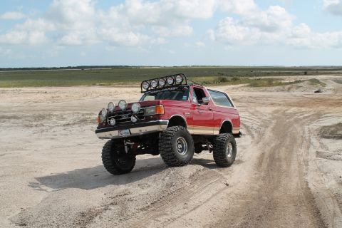 1990 Ford Bronco - A modified 1987 Ford Bronco navigates a sandy track under a cloudy sky.