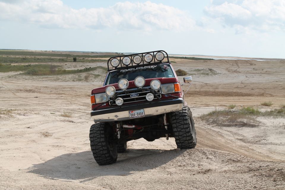Red 1990 Ford Bronco with roof and bumper lights driving on sand