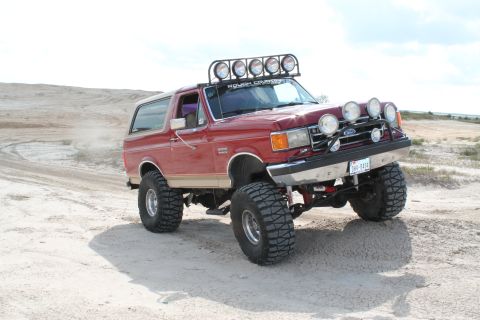 1990 Ford Bronco - This lifted Ford Bronco is kicking up dust as it navigates a sandy terrain.
