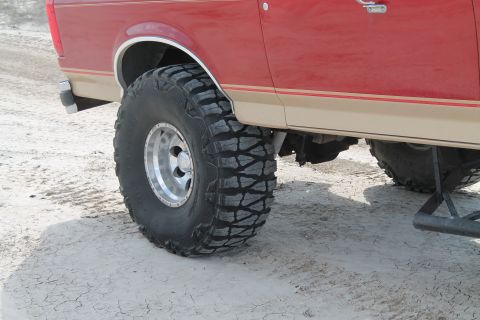 1990 Ford Bronco - Side view of a red and tan SUV large off-road tires. The vehicle appears to be a 1990 Ford Bronco.