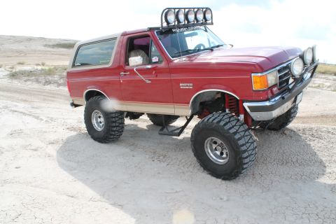 1990 Ford Bronco - This red 1990 Ford Bronco features a lifted suspension, large off-road tires, and a light bar on the roof.