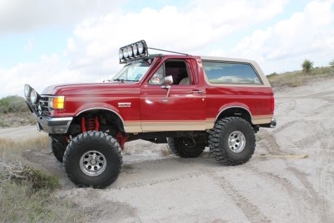 1990 Ford Bronco - A modified 1990 Ford Bronco is shown off-road, equipped with large tires and auxiliary lighting.