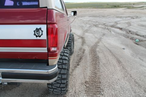 1990 Ford Bronco - Rear view of a red and tan SUV with off-road tires, a skull gear sticker on the side panel.