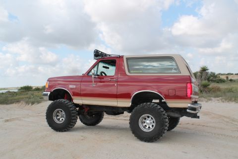 1990 Ford Bronco - Red 1990 Ford Bronco modified with off-road tires and suspension, parked on sand.