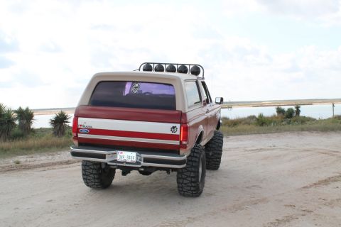 1990 Ford Bronco - A lifted 1990 Ford Bronco sits on a dirt lot near the water, its rear end angled towards the camera.