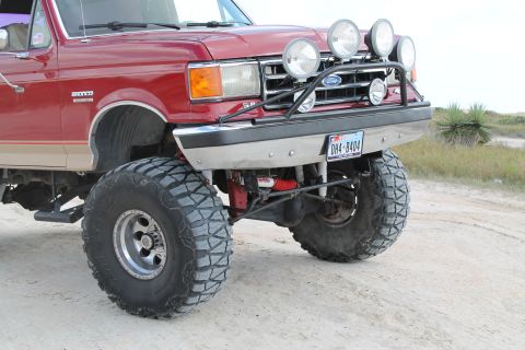 1990 Ford Bronco - This modified Ford truck features a prominent grille guard with multiple spotlights and oversized tires for off-road use.
