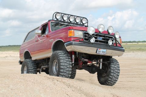 1990 Ford Bronco - This lifted 1990 Ford Bronco is equipped with multiple off-road lights and large tires, ready for adventure on sandy terrain.